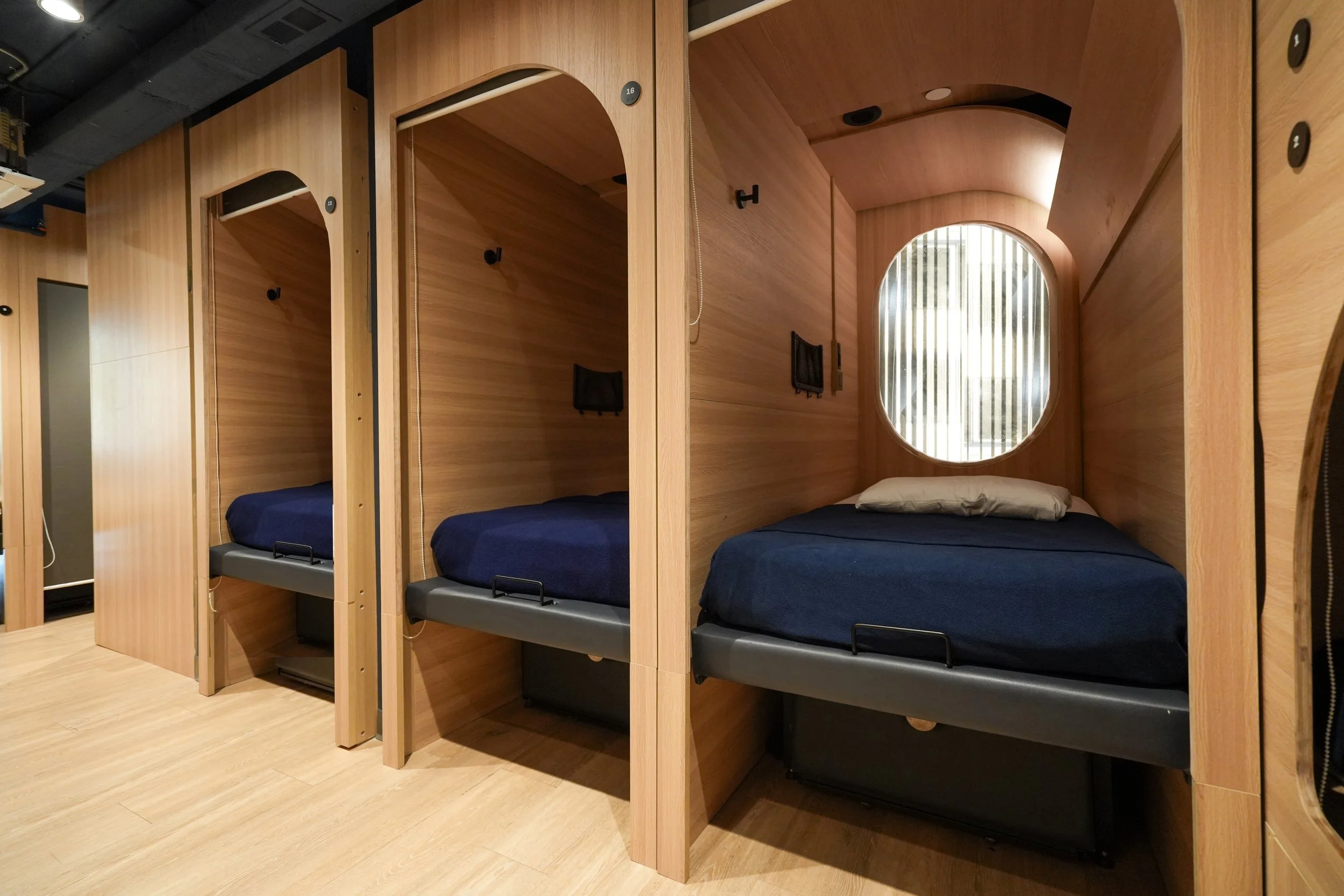 A row of closed sleeping capsules with blinds drawn, in a dimly lit corridor.
